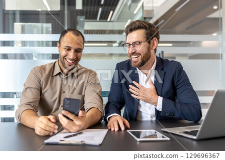 A lively meeting of two colleagues in a modern office, sharing a conversation while using a smartphone for collaboration. 129696367