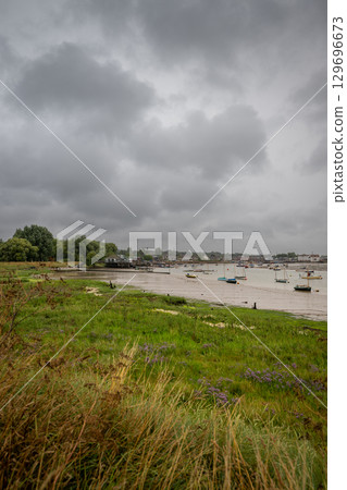 River Deben at low tide with small boats under a stormy sky. View towards the historic town of Woodbridge in Suffolk, UK. River Deben at low tide with small boats under a stormy sky. View towards the historic town of Woodbridge in Suffolk, UK. 129696673