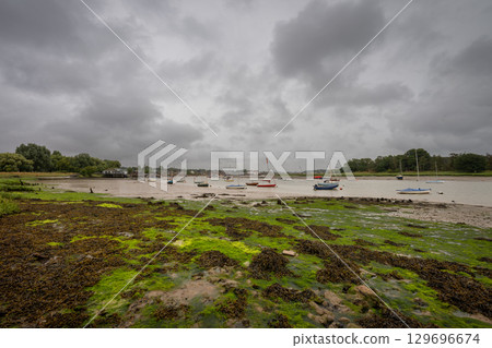 River Deben at low tide with small boats under a stormy sky. View towards the historic town of Woodbridge in Suffolk, UK. River Deben at low tide with small boats under a stormy sky. View towards the historic town of Woodbridge in Suffolk, UK. 129696674
