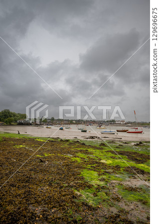 River Deben at low tide with small boats under a stormy sky. View towards the historic town of Woodbridge in Suffolk, UK. 129696675