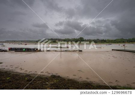 River Deben at low tide with small boats under a stormy sky. View across the river near the historic town of Woodbridge in Suffolk, UK. River Deben at low tide with small boats under a stormy sky. View across the river near the historic town of Woodbridge in Suffolk, UK. 129696678