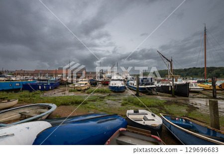 Small boats under a stormy sky. View of the quay at low tide on the River Deben in the historic town of Woodbridge in Suffolk, UK. 129696683