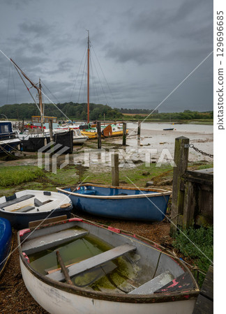 Small boats under a stormy sky. View of the quay at low tide on the River Deben in the historic town of Woodbridge in Suffolk, UK. 129696685