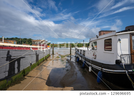 Boats sitting on mud in sunshine. View of the quay at low tide on the River Deben in the historic town of Woodbridge in Suffolk, UK. Boats sitting on mud in sunshine. View of the quay at low tide on the River Deben in the historic town of Woodbridge in Suffolk, UK. 129696695