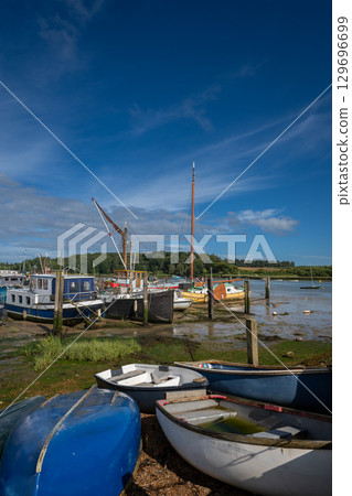 Small boats on a sunny day. View of the quay at low tide on the River Deben in the historic town of Woodbridge in Suffolk, UK. Small boats on a sunny day. View of the quay at low tide on the River Deben in the historic town of Woodbridge in Suffolk, UK. 129696699
