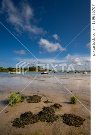 River Deben at low tide with small boats on a sunny day. View near the historic town of Woodbridge in Suffolk, UK. River Deben at low tide with small boats on a sunny day. View near the historic town of Woodbridge in Suffolk, UK. 129696707