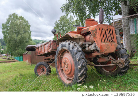 Vintage red old tractor t16 parked in a lush green field near a rustic farmhouse on a cloudy day in the countryside 129697536