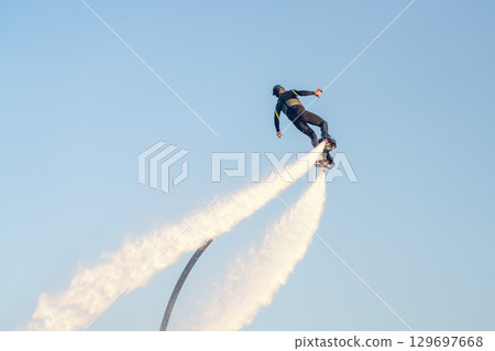 Flyboard enthusiast soars high above the water, propelled by powerful jets of water shooting from the board. The stunning backdrop features a clear blue sky, enhancing excitement of this water sport. 129697668
