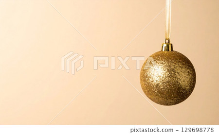 Golden Christmas Ball Ornament Hanging on Beige Background for Festive Season 129698778