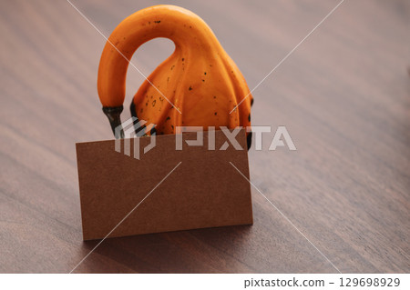 Small two tone decorative pear shaped pumpkin on black walnut table with empty paper card 129698929