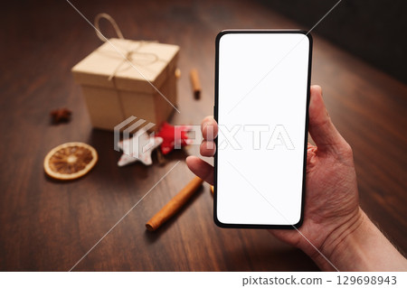 Man hand hold smarthone with white screen with christmas decorations on background 129698943