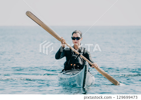 Woman sea kayak. Happy smiling woman in kayak on ocean, paddling with wooden oar. Calm sea water and horizon in background. Active lifestyle at sea. Summer vacation. Woman sea kayak. Happy smiling woman in kayak on ocean, paddling with wooden oar. Calm sea water and horizon in background. Active lifestyle at sea. Summer vacation. 129699473