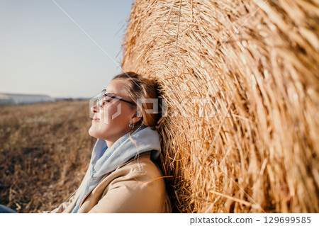 Smiling Woman Resting Against Hay Bale 129699585