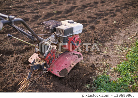 Garden tiller machine working on soil in sunny outdoor setting for farming 129699963