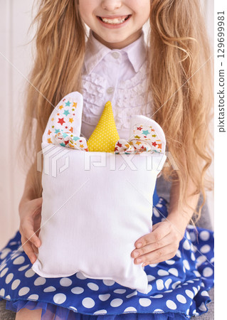 Smiling caucasian female child holding bunny pillow in polka dot skirt inside 129699981