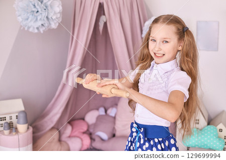Caucasian female child baking pretend play in bedroom with rolling pin 129699994