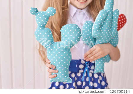 Smiling caucasian young girl holding handmade polka dot cactus toys in blue 129700114