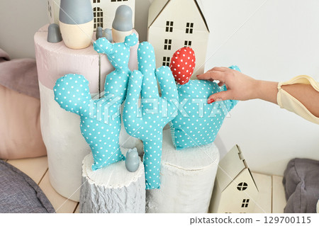 Female hand arranging polka dot cactus cushions among miniature wooden houses Female hand arranging polka dot cactus cushions among miniature wooden houses 129700115