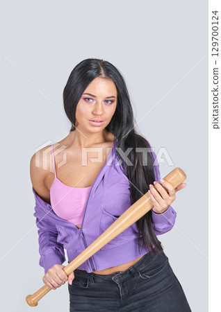 Young caucasian female holding baseball bat in casual pink and purple outfit 129700124