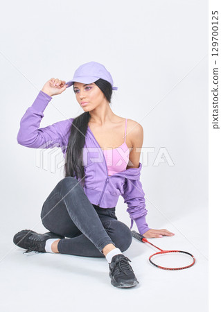 Young caucasian female in casual sportswear with tennis racket sitting on floor 129700125