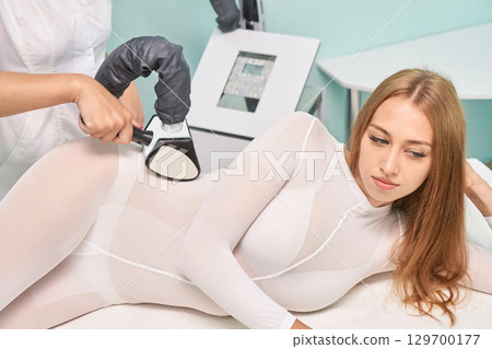 Young caucasian female receiving body sculpting treatment in spa with modern Young caucasian female receiving body sculpting treatment in spa with modern 129700177