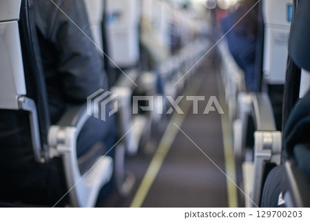 Blurred interior view of airplane aisle with rows of seats and passengers Blurred interior view of airplane aisle with rows of seats and passengers 129700203