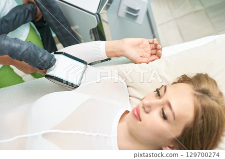 Young caucasian woman receiving laser hair removal treatment on arm in clinic Young caucasian woman receiving laser hair removal treatment on arm in clinic 129700274