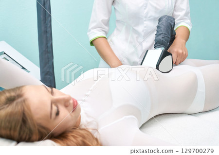 Female caucasian young woman undergoing non-invasive body sculpting treatment 129700279