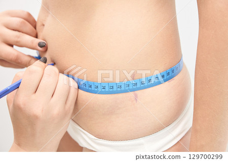 Close-up of measuring tape on caucasian young female s waist for fitness 129700299