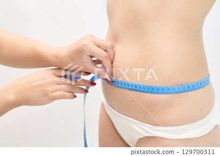 Female waist measurement with blue tape for fitness and health 129700311