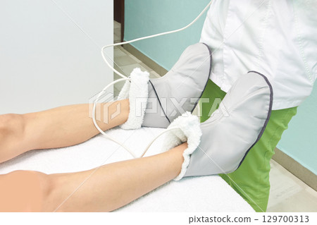 Female adult undergoing heat therapy with electric mittens on legs in a spa 129700313