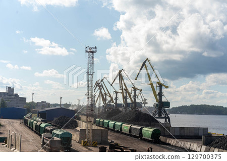 Industrial port with cranes, trains, and large piles of coal, illustrating a logistics and cargo hub Industrial port with cranes, trains, and large piles of coal, illustrating a logistics and cargo hub 129700375