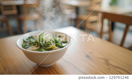 A steaming bowl of delicious ramen on a wooden table in a cozy restaurant setting A steaming bowl of delicious ramen on a wooden table in a cozy restaurant setting 129701246