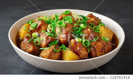 Delicious Chicken Adobo with Tender Potatoes and Fresh Green Onions Served in a Bowl on a Dark Background 129701418