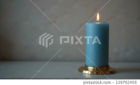 Elegant blue candle with flickering flame on a golden holder in a serene setting exudes calmness 129702458