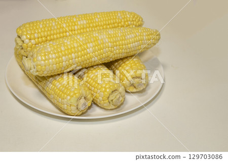 Raw cobs of sweet corn on plate against background. Tasty sweet corn on cobs Raw cobs of sweet corn on plate against background. Tasty sweet corn on cobs 129703086