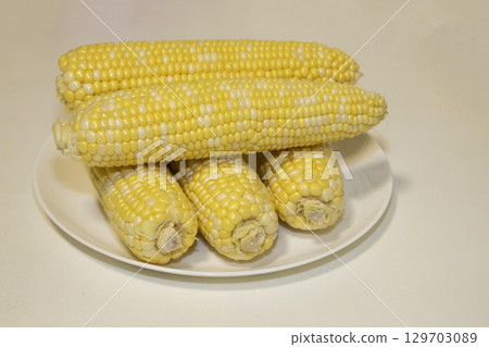 Raw cobs of sweet corn on plate against background. Tasty sweet corn on cobs Raw cobs of sweet corn on plate against background. Tasty sweet corn on cobs 129703089