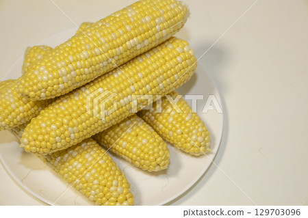 Raw cobs of sweet corn on plate against background. Tasty sweet corn on cobs Raw cobs of sweet corn on plate against background. Tasty sweet corn on cobs 129703096