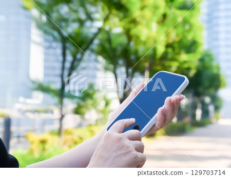 A woman operating a smartphone outdoors A woman operating a smartphone outdoors 129703714