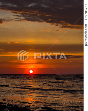 Beautiful sunset over the ocean with vibrant colors reflecting on calm waves at a coastal location 129703754
