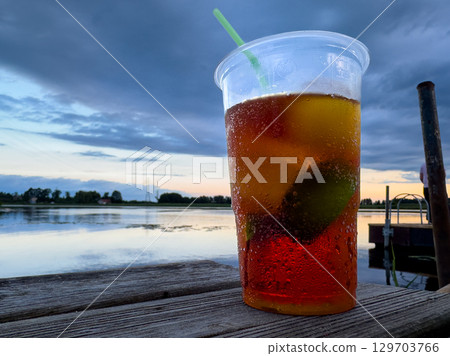 Refreshing beverage by the water at sunset, showcasing vibrant colors and evening tranquility 129703766