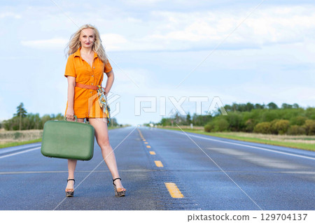Blonde woman with a green retro suitcase standing on the highway. Blonde woman with a green retro suitcase standing on the highway. 129704137