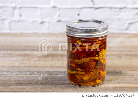 Yellow and red dried tomatoes in a jar with herbs and oil. Yellow and red dried tomatoes in a jar with herbs and oil. 129704154