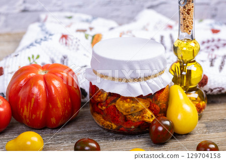 Dried tomatoes in a jar and ingredients on the kitchen table. 129704158