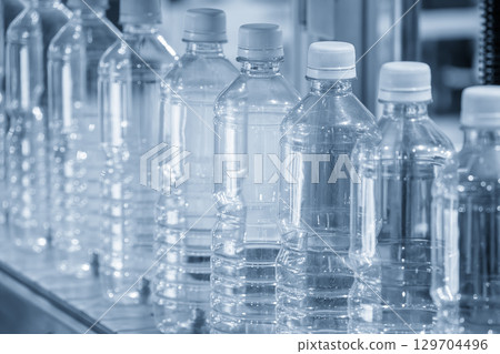 The full filled drinking water bottles  on the conveyor belt in the blue tone scene. 129704496