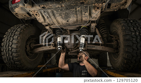 mechanic works on lifted vehicle, inspecting and replacing shock absorbers 129705120