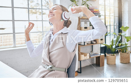 Music, headphones and senior business woman dance in office, happy and excited about small business. Earphones, dancing and elderly female celebrate in design studio, cheerful and positive at a desk 129705651