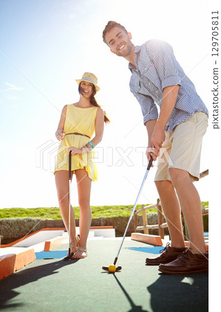 Couple, mini golf and happy man with club, smile and hit ball on date, fun activity and freedom in sunshine. Excited young people playing outdoor putt putt with bat, summer happiness and grass turf Couple, mini golf and happy man with club, smile and hit ball on date, fun activity and freedom in sunshine. Excited young people playing outdoor putt putt with bat, summer happiness and grass turf 129705811