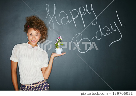 Black woman, studio portrait and holding plant with smile, beauty and celebration of birthday. Woman, teacher and writing wall for happy birthday, b-day and happiness with flowers for gift of growth 129706031
