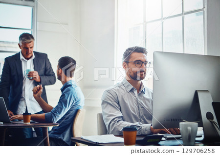 Computer, work and businessman with his colleagues in the background talking, speaking and planning. Pc, success and professional male employee working on a corporate company report in the office. 129706258
